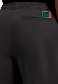 Gli shorts sportivi neri presentano un elastico in vita, una tasca posteriore con cucitura piatta e un'etichetta logo colorata in rosa e verde.