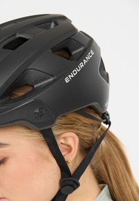 Schwarzer Fahrradhelm mit Belüftungsöffnungen und verstellbaren Riemen. Auf der Seite steht das Wort "ENDURANCE". Mattes Finish, stromlinienförmiges Design, leicht.