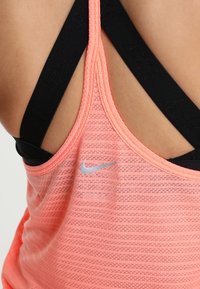 Débardeur de sport rose avec un motif texturé, doté de bretelles noires et d'un petit logo Nike argenté sur le devant.