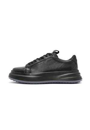 Black leather sneaker featuring a smooth finish, rounded toe, lace-up front, and a thick, textured sole with a slight heel.