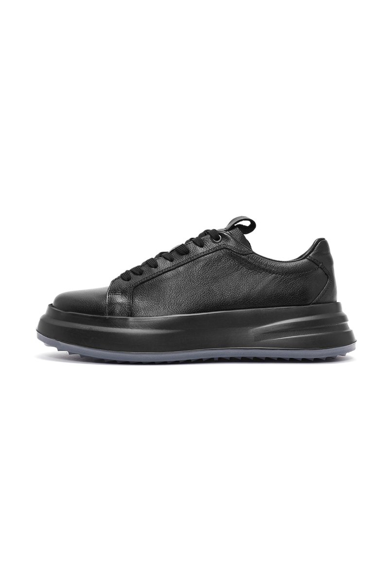 Sneaker in pelle nera con finitura liscia, punta rotonda, stringatura frontale e suola spessa e texture con un leggero tacco.