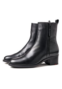 Paire de bottines en cuir noir avec fermetures éclair latérales, talons bloc, et languettes à l'arrière sur fond blanc.