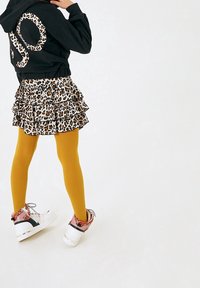 Black hoodie with leopard print number, layered leopard print skirt, mustard yellow tights, and high-top sneakers with pink and white accents.