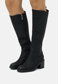 Botas negras hasta la rodilla de suave ante con un tacón grueso, que cuentan con una cremallera lateral y sutiles detalles texturizados.