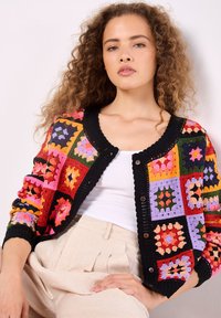 Mehrfarbige Häkeljacke mit quadratischem Muster und schwarzem Besatz. Hergestellt aus Garn, hat sie Knöpfe vorne und eine strukturierte Oberfläche.