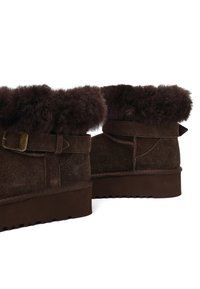 Braune Wildleder-Stiefeletten mit einem flauschigen Pelzsaum, Schnallendetail, strukturiertem Sohlenprofil und einem stabilen Keilabsatz.