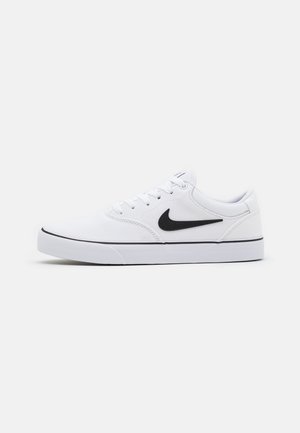 Baskets basses blanches avec le swoosh Nike noir, lacets blancs et une fine ligne noire au-dessus de la semelle en caoutchouc blanche.