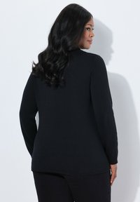 Schwarzes langärmliges Strickoberteil mit abgerundetem Saum und strukturiertem Stoff, von hinten betrachtet. Der Schnitt ist locker und zeigt ein einfaches, klassisches Design.