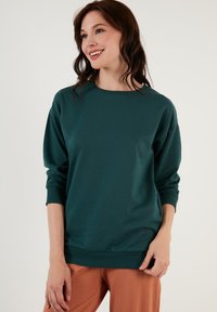 Felpa teal con collo rotondo e vestibilità comoda. Presenta polsini e orlo a coste, realizzata in morbido tessuto di cotone. Design e texture casual.