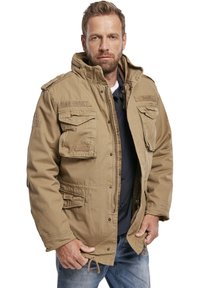 Jachetă bej de stil militar, cu multiple buzunare frontale, guler înalt și închidere cu fermoar. Materialul are un aspect texturat.