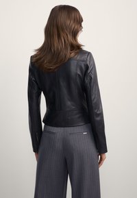 Czarna skórzana kurtka o dopasowanym kroju, z długimi rękawami i skróconą talią. Połączona z szarymi spodniami w prążki o gładkiej fakturze.