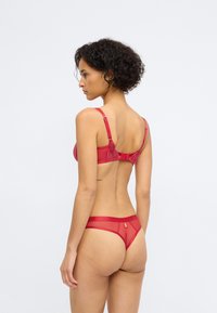Conjunto de sutiã e fio dental vermelho feito de renda transparente e tecido suave. Apresenta alças ajustáveis, um fecho de gancho e olho, e um design minimalista.