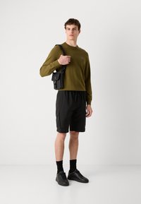 Cameră verde de măsline cu mânecă lungă, pantaloni scurți cargo negri, adidași negri și o geantă mică neagră tip crossbody. Material neted, croială lejeră.