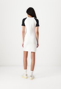 White short-sleeve dress with black raglan sleeves, slim fit, made from soft fabric. Paired with white sneakers and ankle socks.
