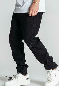 Jeans de mezclilla negra con un corte ajustado, que presentan detalles desgastados y cinco bolsillos, combinados con zapatillas blancas y una camiseta blanca sencilla.