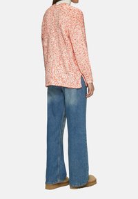 Modischer Pullover mit langen Ärmeln aus einem strukturierten weißen Strick mit orangefarbenen Sprenkeln, kombiniert mit weit geschnittenen blauen Jeans und hellbraunem Schuhwerk.
