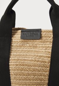 Woven straw tote bag with black fabric handles and a dark label. Features a textured, natural straw body with a geometric pattern.