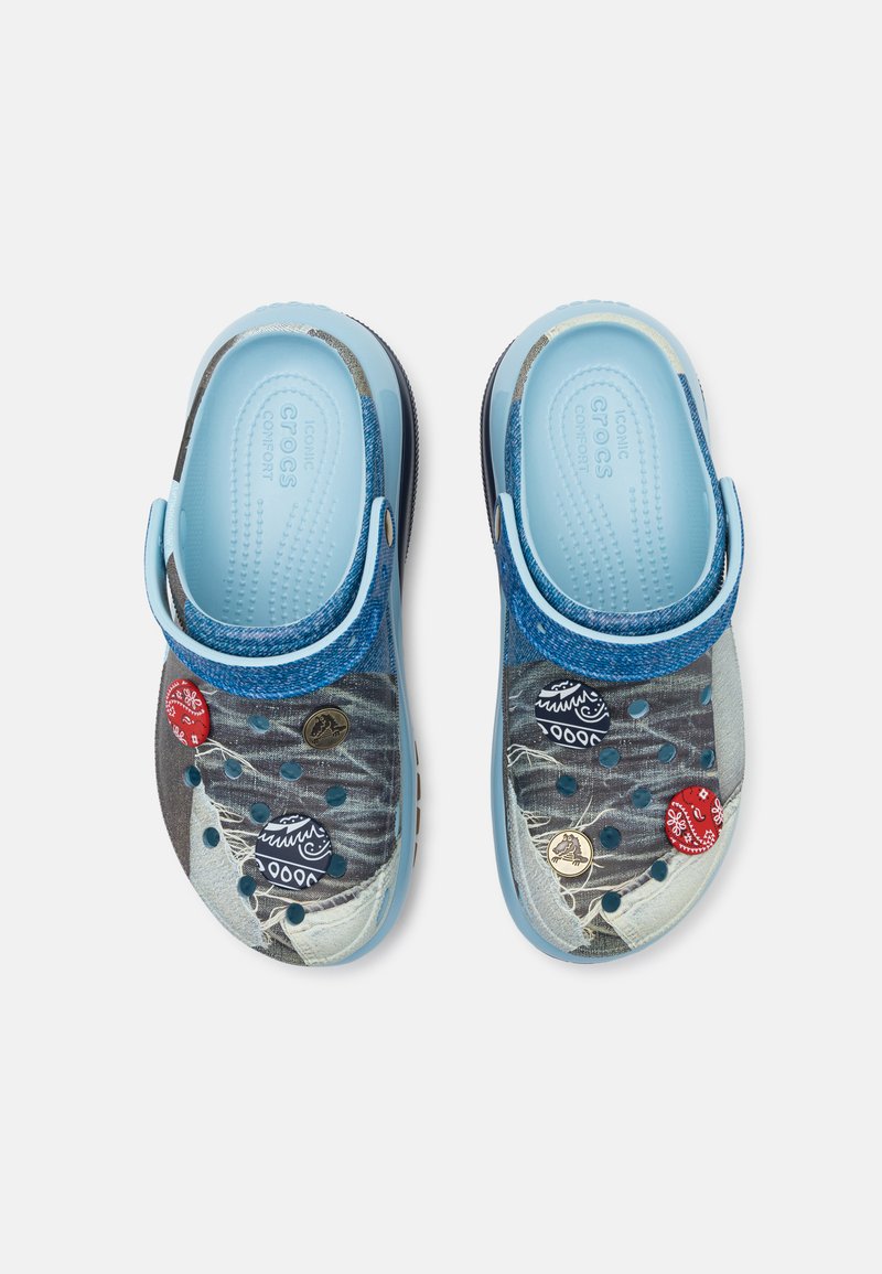 Zuecos azules con un diseño estampado y correa trasera ajustable, que cuentan con un suave forro interior y distintivos decorativos de colores en la superficie.