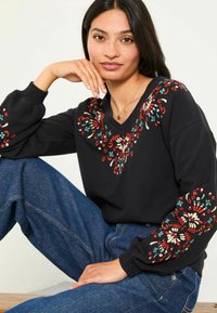 Schwarzer Sweater mit buntem floralem Stickerei entlang des Halsausschnitts und der Ärmel, im entspannten Schnitt und mit V-Ausschnitt.