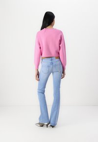 Rosa kortärmad tröja med långa ärmar, kombinerad med ljusblå utsvängda jeans. Outfiten har en enkel design och inga synliga mönster.