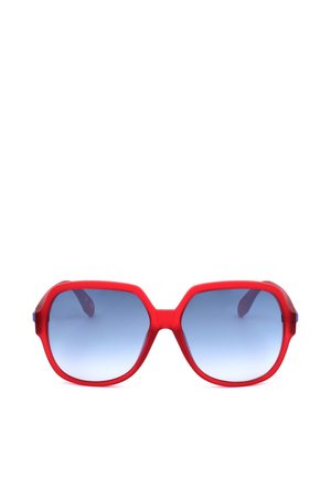 Occhiali da sole in plastica rossa con grandi lenti esagonali sfumate blu e montature spesse mostrati su sfondo bianco.