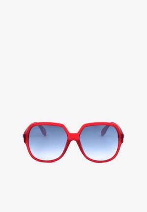 Occhiali da sole in plastica rossa con grandi lenti esagonali sfumate blu e montature spesse mostrati su sfondo bianco.
