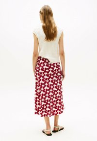 Gehaakte witte mouwloze top gecombineerd met een middellange rok met een rood bloemenpatroon op een witte achtergrond. Platte sandalen maken de look af.