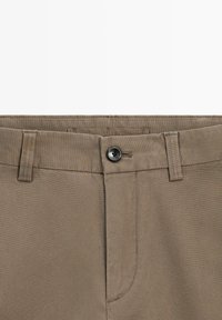 Brune bomuldsbukser med en glat tekstur, der har lukning med sort knap, bæltestropper og sidelommer.