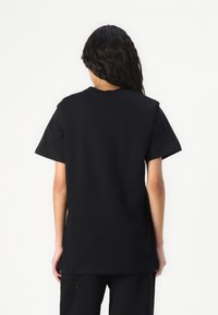 Sort kortærmet t-shirt med en afslappet pasform, rund halsudskæring og glat bomuldsstruktur. Bagfra ses et minimalistisk design uden synlig branding.
