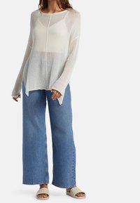 Leichter, gerippter, cremfarbener Pullover mit langen Ärmeln, kombiniert mit weit geschnittenen blauen Jeans und sandfarbenen, geflochtenen Slides, die eine lockere Passform haben.