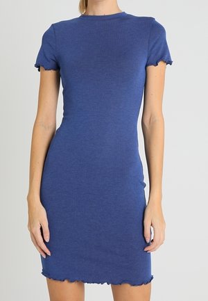 Dopasowana niebieska dzianinowa sukienka z krótkim rękawem, z zakończeniami w falbę na rękawach i na dole, noszona przez stojącą osobę na jednolitym tle.