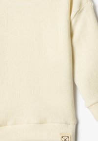 Helles, gelbes Rippenpullover mit langen Ärmeln, der eine weiche Textur und ein kleines Bärenlogo-Label am Saum aufweist.