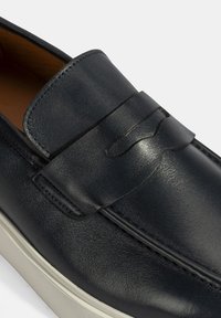 Navy leren instapper met gestikte details en een decoratieve band. Kenmerkt zich door een contrasterende crèmekleurige zool voor extra contrast en stijl.