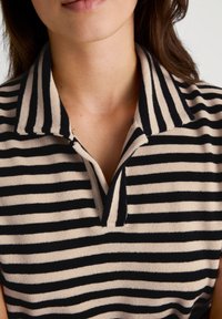 Beige en zwart gestreepte poloshirt met een zachte textuur, voorzien van een kraag en een knoopsluiting met een korte opening bij de hals.