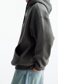 Sudadera gris oscuro hecha de tejido suave, con un gran bolsillo frontal, capucha con cordón y puños acanalados. Con un corte holgado.