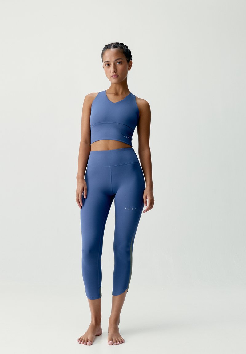 Niebieski zestaw biustonosza sportowego i legginsów wykonany z elastycznego materiału. Biustonosz ma dekolt w kształcie litery V; legginsy mają wycięcia na łydkach.