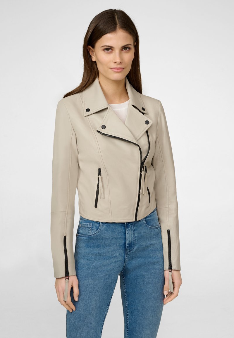 Beige Leder-Motorradjacke mit einer cropped Design, Reißverschluss vorne, zwei seitlichen Taschen und kontrastierenden schwarzen Reißverschlüssen und Hardware-Details.