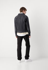 Jeans jakna u tamno sivoj boji s laganim izbljeđelim finišem, u kombinaciji s crnim hlačama. Značajke uključuju klasičan ovratnik i dugmad na manžetama.