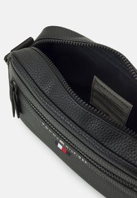 Black synthetic leather bag with a textured surface, zipper closure, and logo detail. Interior is lined with black fabric.