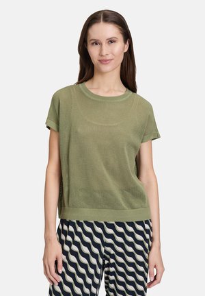 Top court en maille lâche de couleur vert olive avec un col rond et un ourlet côtelé, associé à un pantalon large à motifs bleu marine et crème.