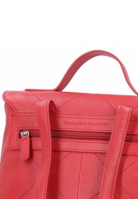 Bolso de cuero rojo con un patrón acolchado, que cuenta con un asa superior y un bolsillo con cremallera, embellecido con "hecho a mano desde 1928."
