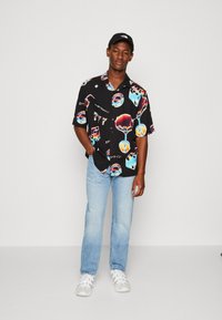 Maglietta nera a maniche corte con motivi astratti colorati e scritte; abbinata a jeans azzurri e sneakers bianche.