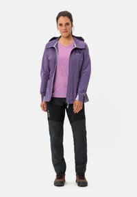Paarse waterdichte jas met een capuchon over een lichtpaarse t-shirt, gecombineerd met zwart en grijs broek. Bruine wandelschoenen maken de outfit compleet.