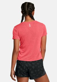 Różowa, krótko rękawowa sportowa bluzka z teksturowanego materiału i odblaskowymi akcentami, zestawiona z czarnymi szortami z subtelnym wzorem.