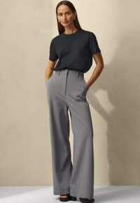 Black short-sleeve t-shirt paired with high-waisted, wide-leg gray trousers. The outfit features a sleek design and minimalistic accents.