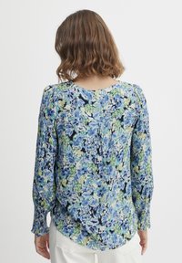 Blumenbluse mit blauen und grünen Mustern auf einem hellen Hintergrund, aus leichtem Stoff, mit langen Ärmeln und Rundhalsausschnitt.
