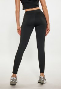 Leggings neri con un alto punto vita, design aderente e texture liscia. Abbinati a scarpe da ginnastica argento con una parte superiore in rete.