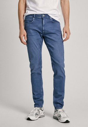 Modri kavbojke s slim fit krojem, petimi žepi, subtilnim zbledelostjo in stikajočimi detajli. Nosi se z svetlo sivimi supergami.