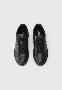 Un paio di sneakers in pelle nere Guess con lacci neri, occhielli in metallo e logo visibile sulla linguetta, viste dall'alto su uno sfondo bianco.