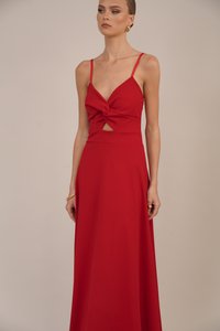 Donna che indossa un abito rosso senza maniche con dettaglio frontale attorcigliato e un piccolo taglio all'altezza del ventre, accessoriato con orecchini a cerchio d'oro e braccialetti.